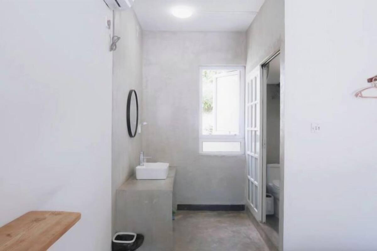 A narrow bathroom with a white sink, a small window, and a door leading to another room.