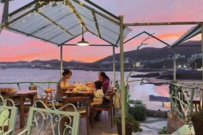 A covered outdoor seating area with tables and chairs, overlooking a body of water and distant hills. - Qingwu Fisherman's Hostel (Shengsi)