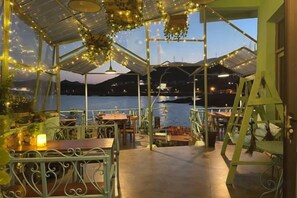 An outdoor dining area with tables and chairs, a covered walkway, and a view of the water. - Qingwu Fisherman's Hostel (Shengsi)