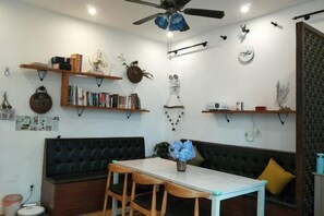 A room with a ceiling fan, a black sofa, a dining table with chairs, and shelves with books and decorative items. - Qingwu Fisherman's Hostel (Shengsi)