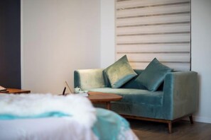 A room with a sofa, a small round table, and a bed with a white bedspread. - Yi She (Chongqing)