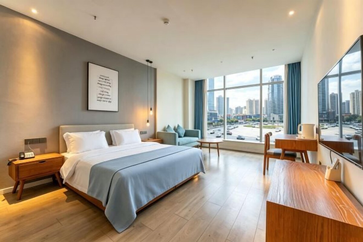 A modern hotel room with a large bed, a desk, and a view of the cityscape.