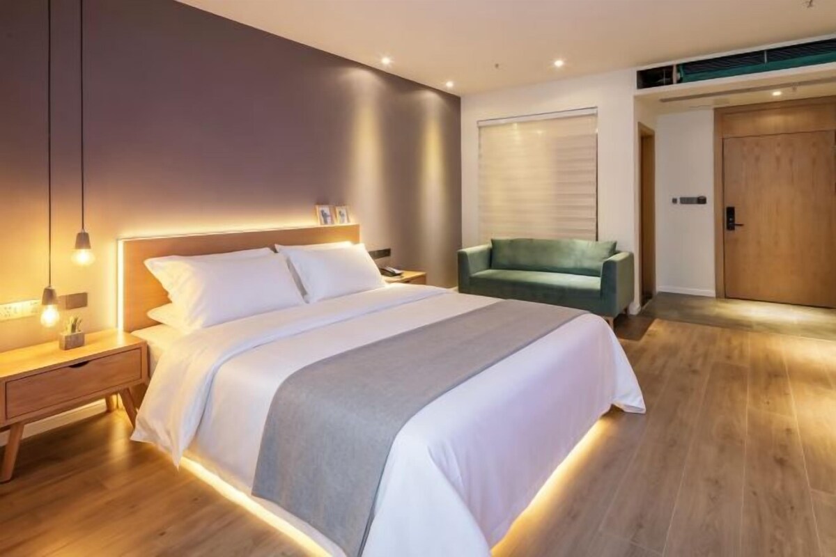 A modern bedroom with a large bed, bedside tables, a green armchair, and a wooden door.