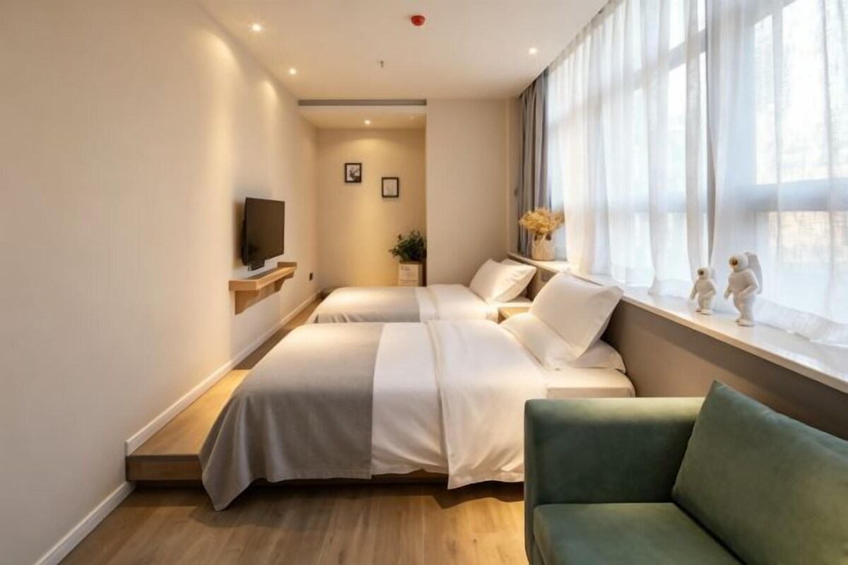 A hotel room with two beds, a green sofa, a TV, and a window with curtains.