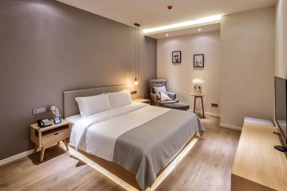 A modern hotel room with a bed, bedside table, nightstand, chair, and a TV.