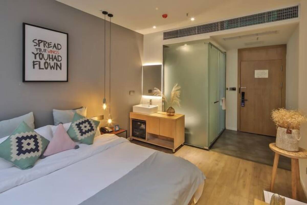 A modern hotel room with a bed, bedside table, lamp, and a mirror.