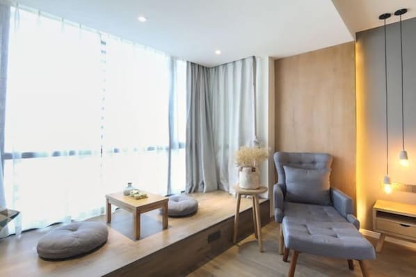 Quarto moderno com sofá, uma pequena mesa, janela com cortinas e luminária fixada na parede.