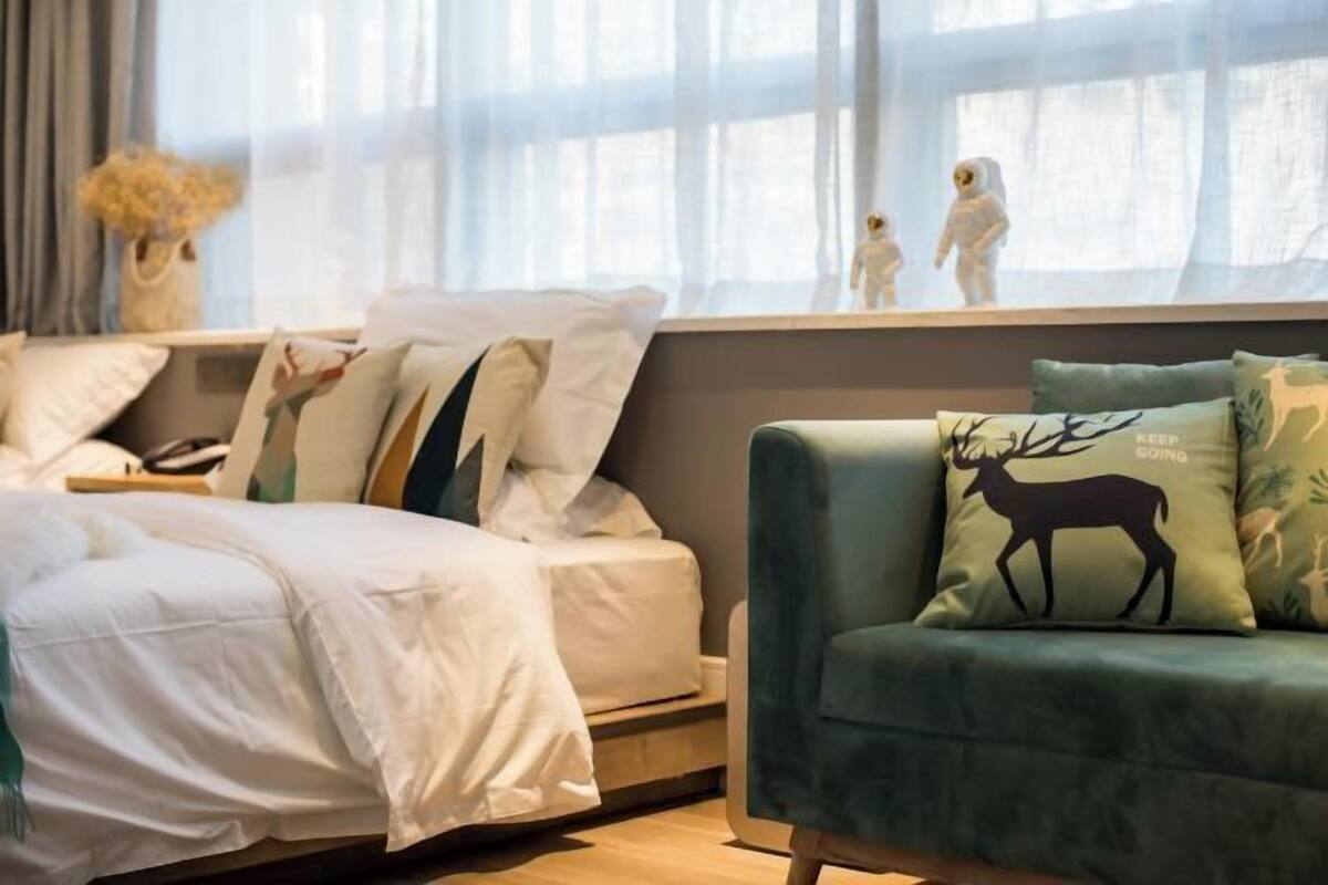 A bedroom with a bed, a green sofa with a deer pillow, and a window with curtains.