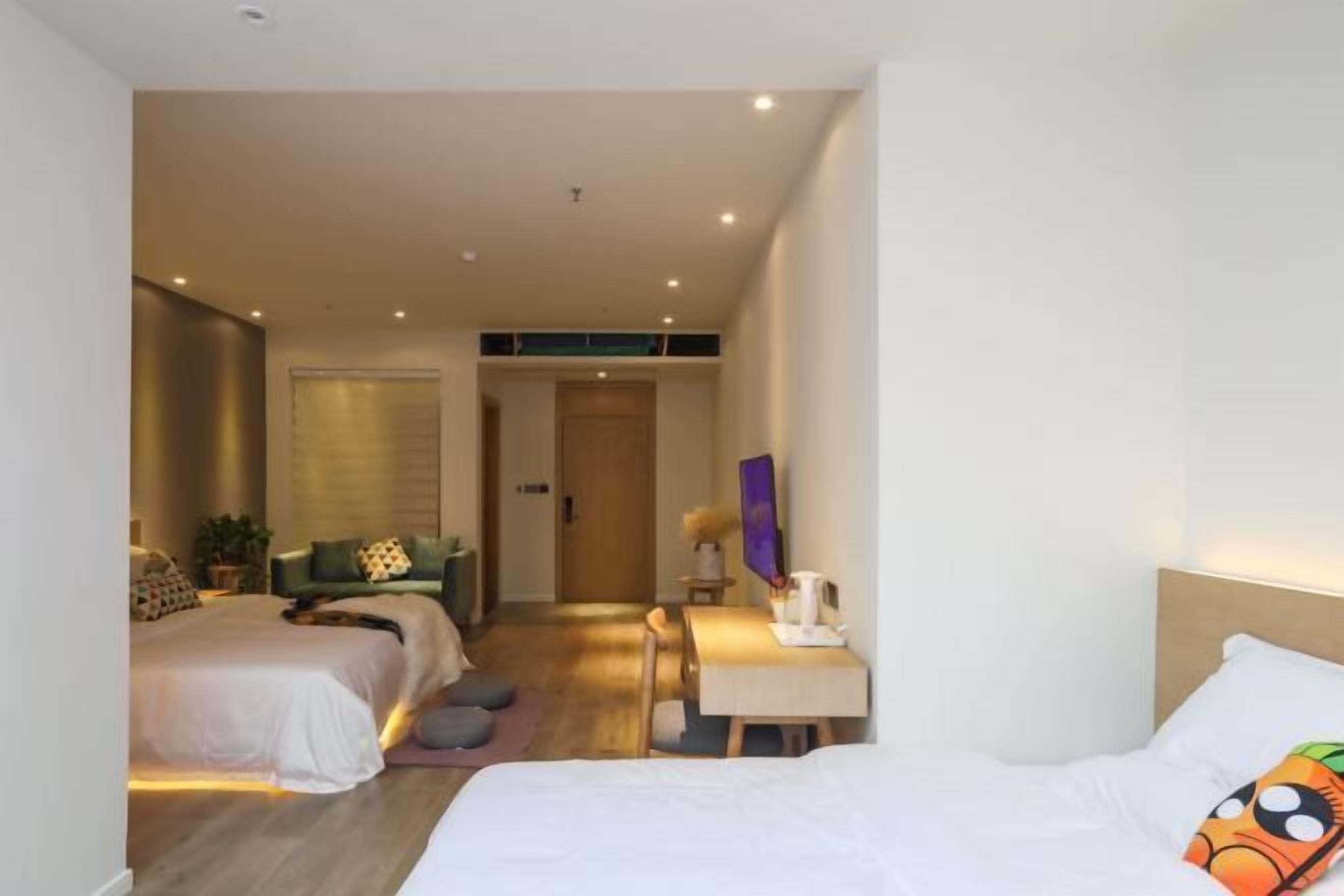 A hotel room with two beds, a desk, a chair, and a small table with a lamp.