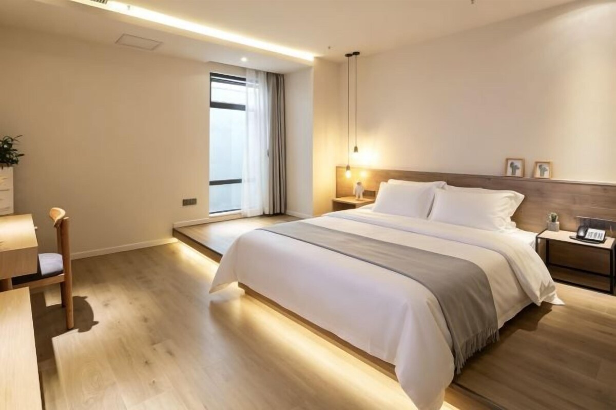 A modern hotel room with a large bed, bedside tables, a desk, and a window with curtains.