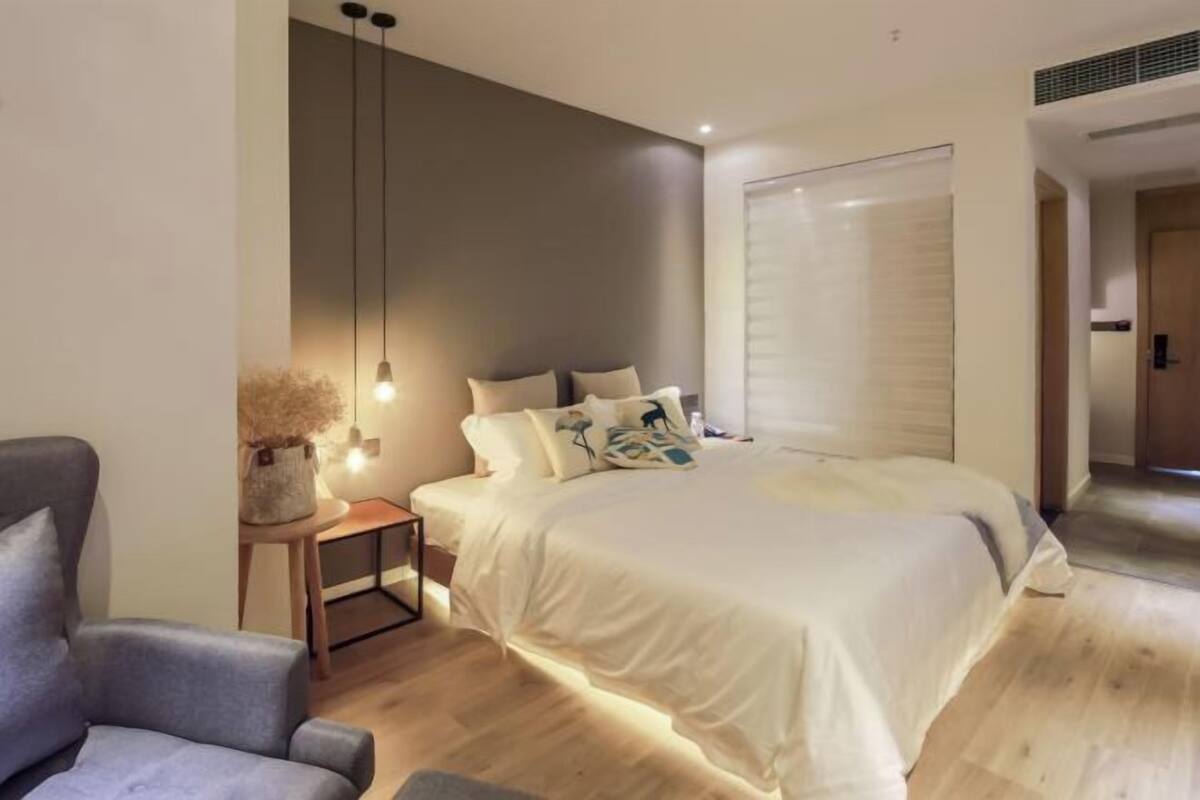 A modern bedroom with a bed, bedside table, lamp, and a chair.