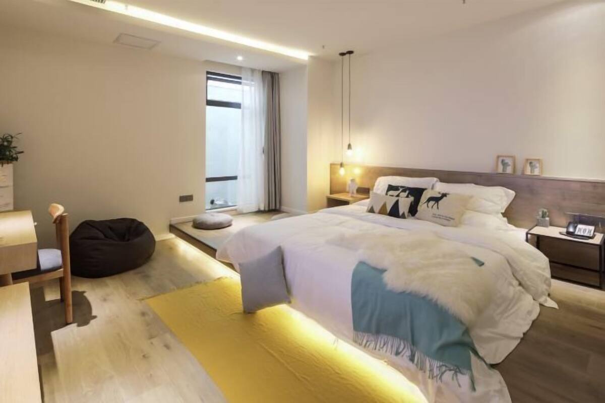 A modern bedroom with a bed, bedside tables, a desk, a chair, and a window.