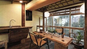 A rustic kitchen with a wooden table, chairs, a sink, and a window with a view of buildings and trees. - Linmusen Hostel (Chongqing Beibei Pedestrian Street Center) (Chongqing)