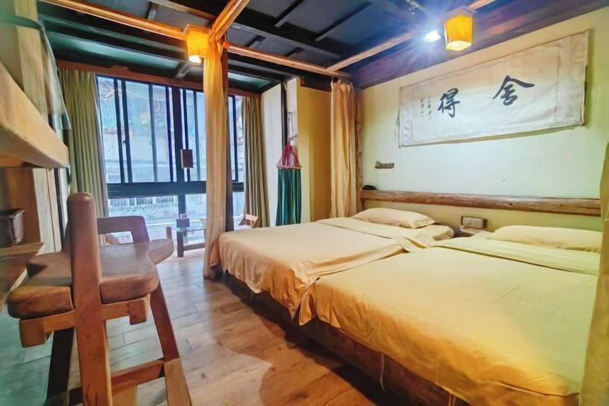 A room with two beds, a wooden chair, a desk, and a large window.