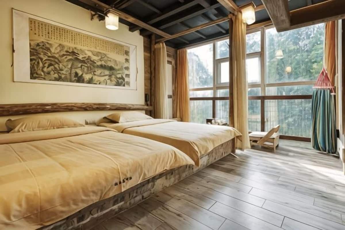 A room with two beds, a large window, and a traditional painting on the wall.