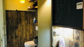 Un baño con pared de madera, inodoro, lavamanos y espejo.