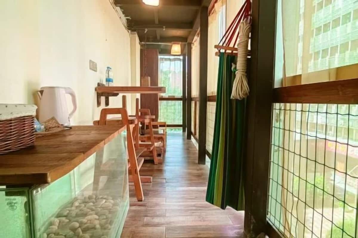 A corridor with wooden flooring, a table with chairs, a water dispenser, and a window with a view of greenery.