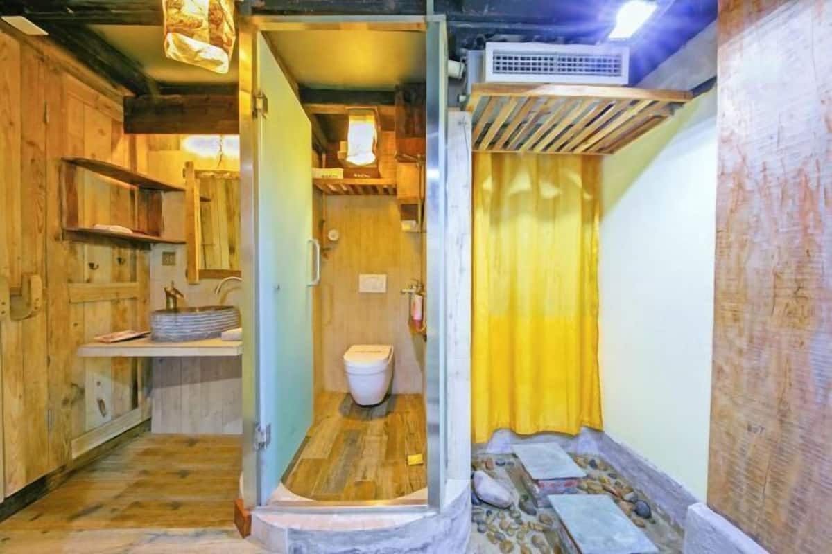 A compact bathroom with a wooden floor, a white toilet, and a yellow shower curtain.