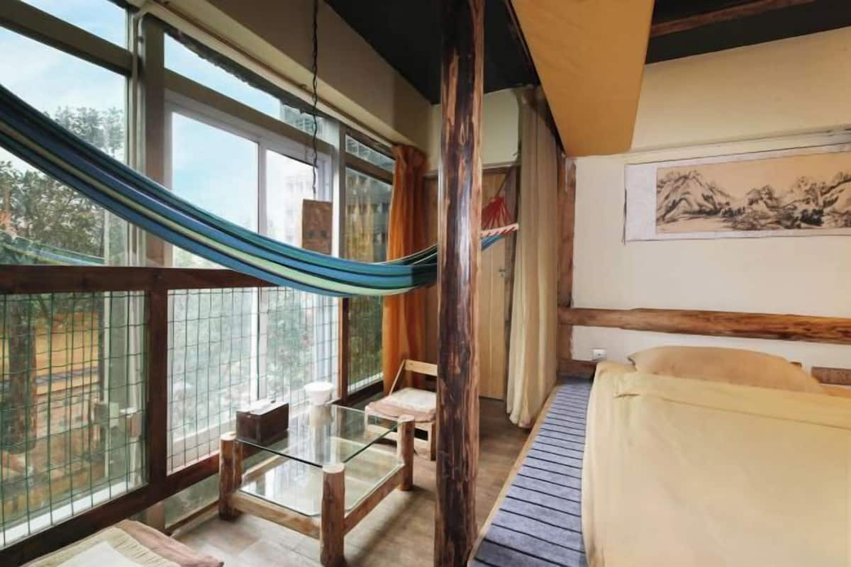 A room with a glass table, a hammock, a bed, and a painting on the wall.