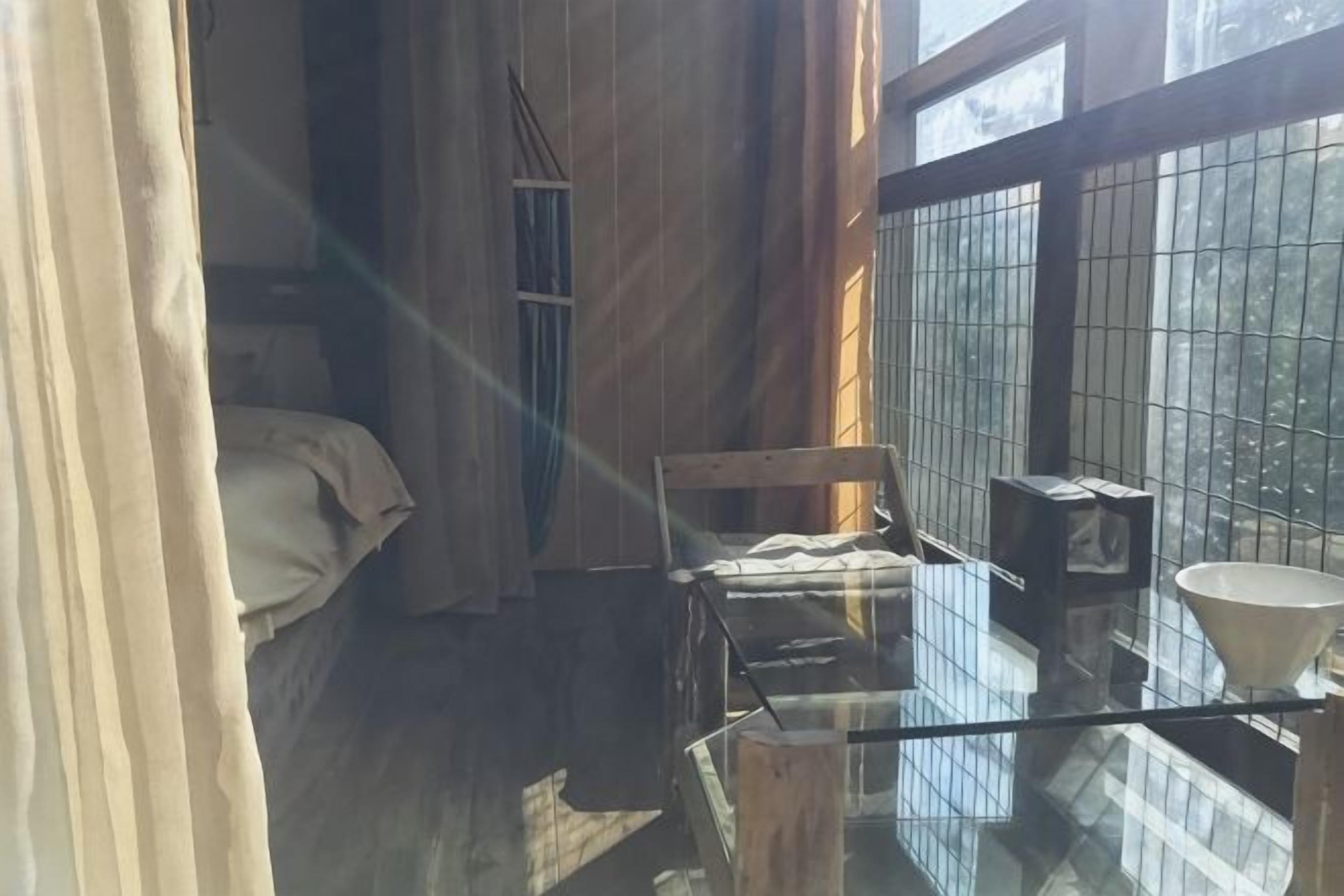 Una stanza con un letto, un tavolino, una sedia e una finestra vista alberi.