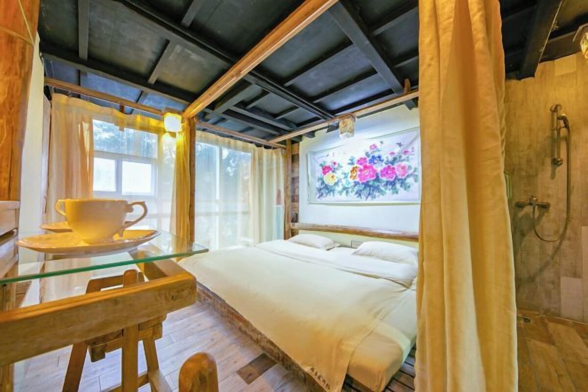 Una habitación con una cama, una mesita de vidrio con una taza y una ventana con cortinas.