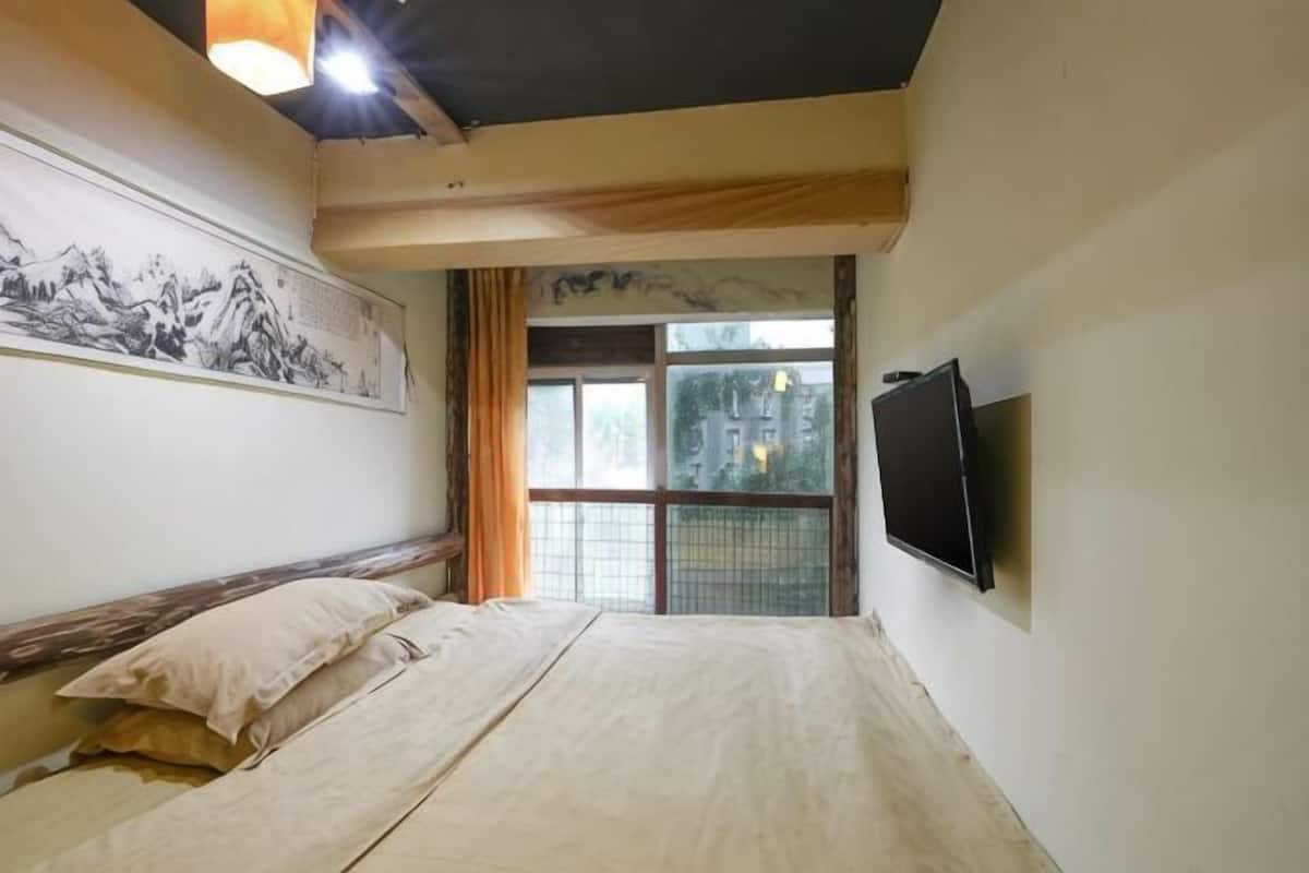 A bedroom with a bed, a television, a window with curtains, and a painting on the wall.