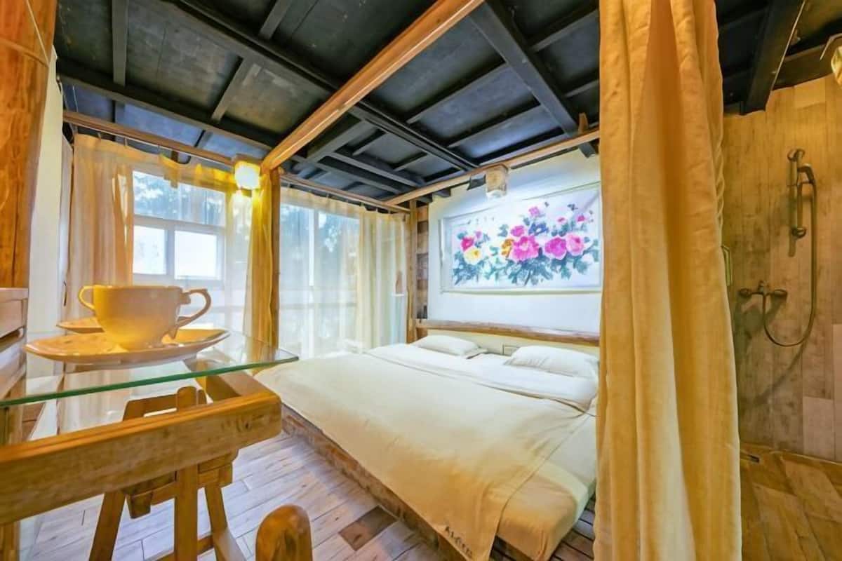 A cozy room with a bed, a glass table with a cup, and a window with curtains.