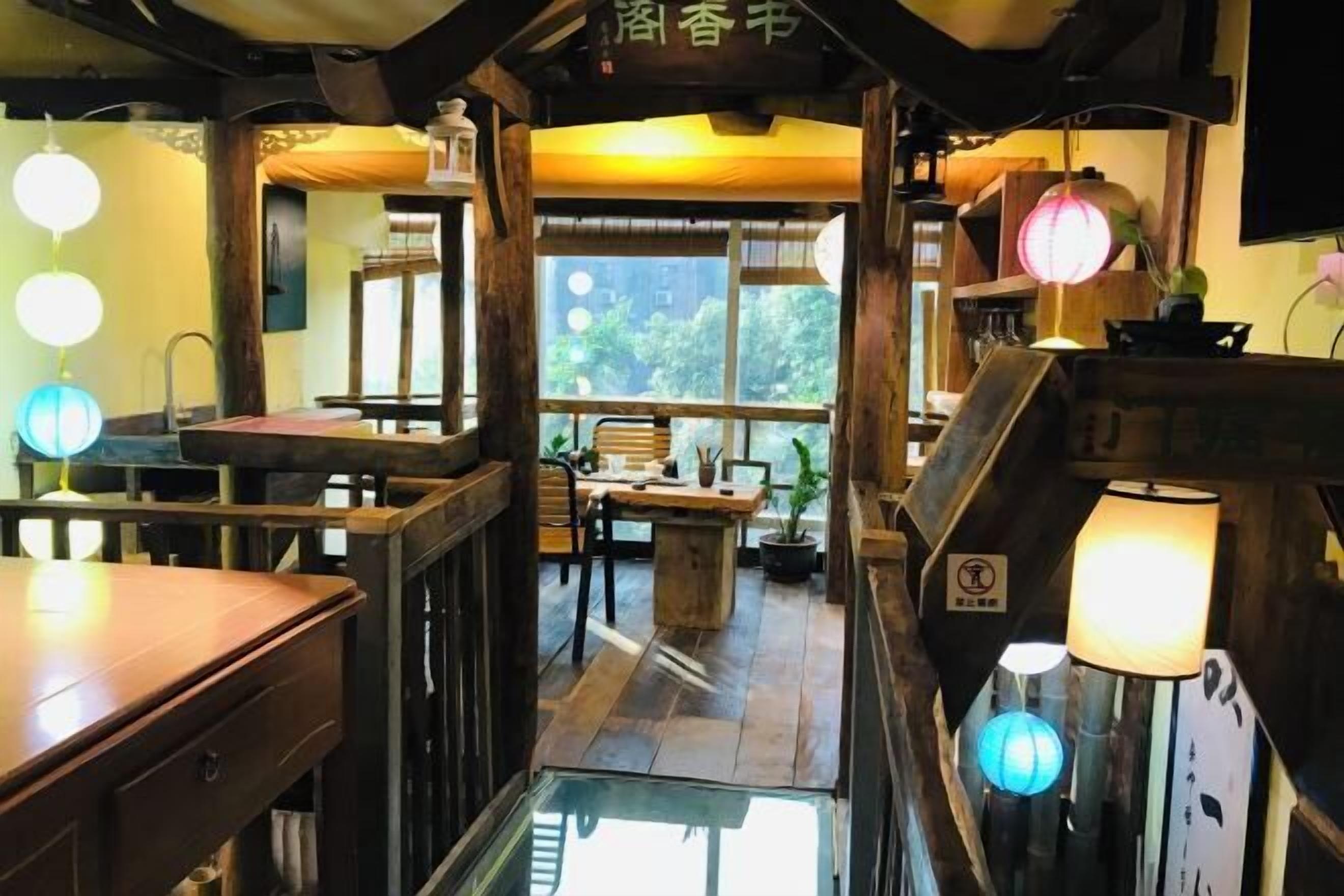 A traditional Japanese-style interior with wooden furniture, hanging paper lanterns, and a view of greenery outside.