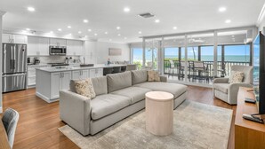 Una cocina moderna con armarios blancos y electrodomésticos de acero inoxidable, un sofá seccional gris y una mesa de centro redonda de madera.