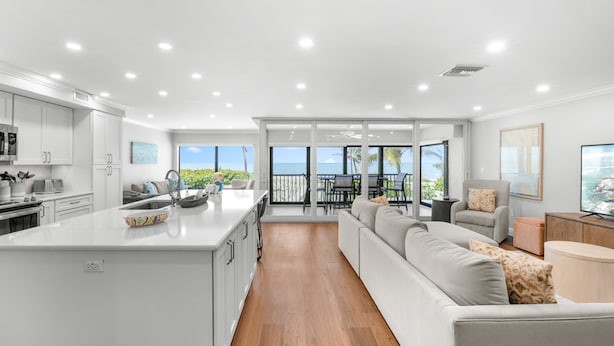 Una cocina moderna con armarios blancos, una isla grande y una zona de comedor con vista al océano.