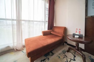 Una habitación con sofá, una mesita redonda con botellas y una ventana con cortinas traslúcidas.
