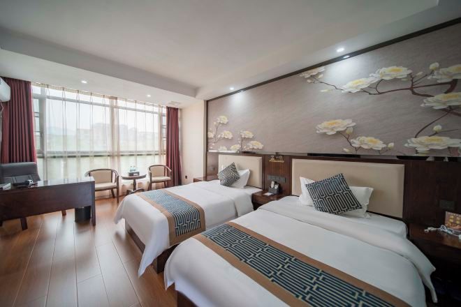 Habitación de hotel con dos camas, un escritorio, una silla y un ventanal grande.