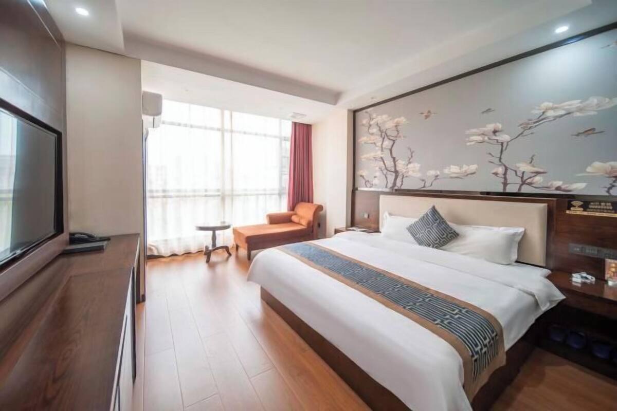 Une chambre d’hôtel avec un grand lit, une télévision, une petite table, une chaise et une fenêtre avec des rideaux.
