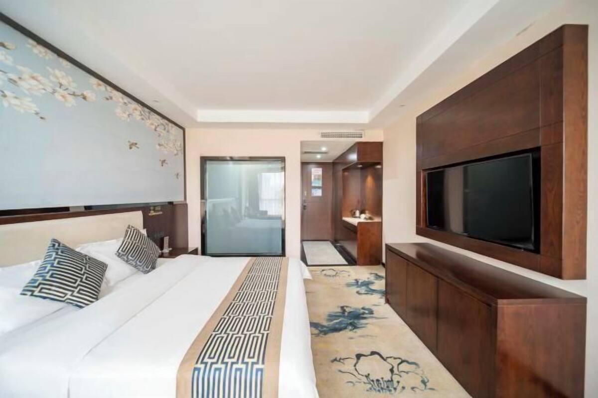 Une chambre d’hôtel comprenant un lit, un téléviseur fixé au mur, une salle de bain avec un miroir et un espace douche.