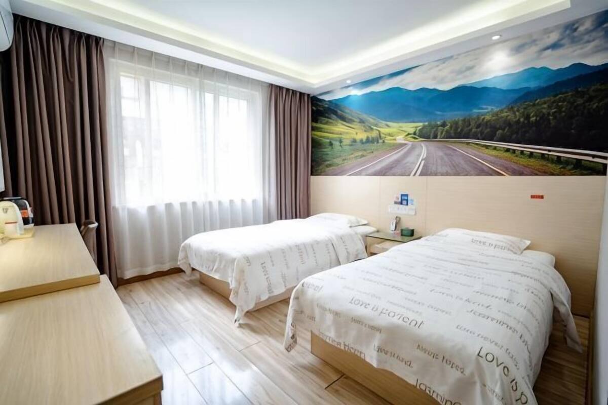 A hotel room with two beds, a desk, a window with curtains, and a painting of a road.