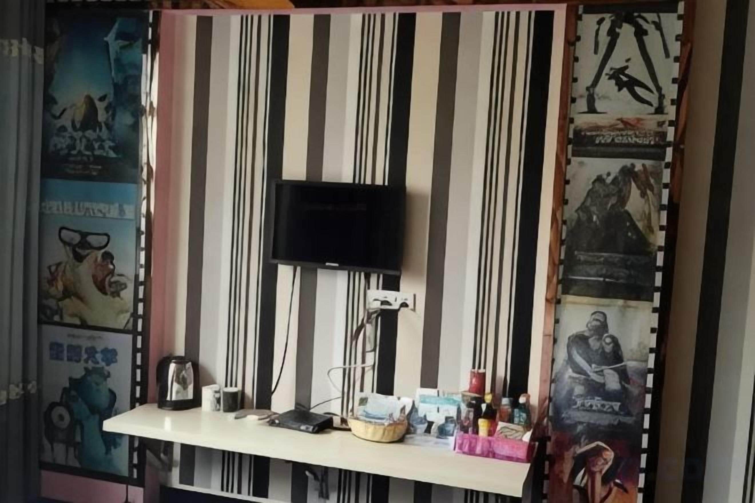 Una habitación con una televisión montada en la pared, un escritorio con varios objetos y carteles en las paredes.