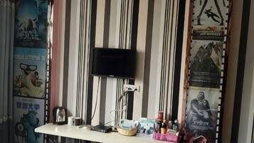 Una habitación con una televisión montada en la pared, un escritorio con varios objetos y carteles en las paredes.