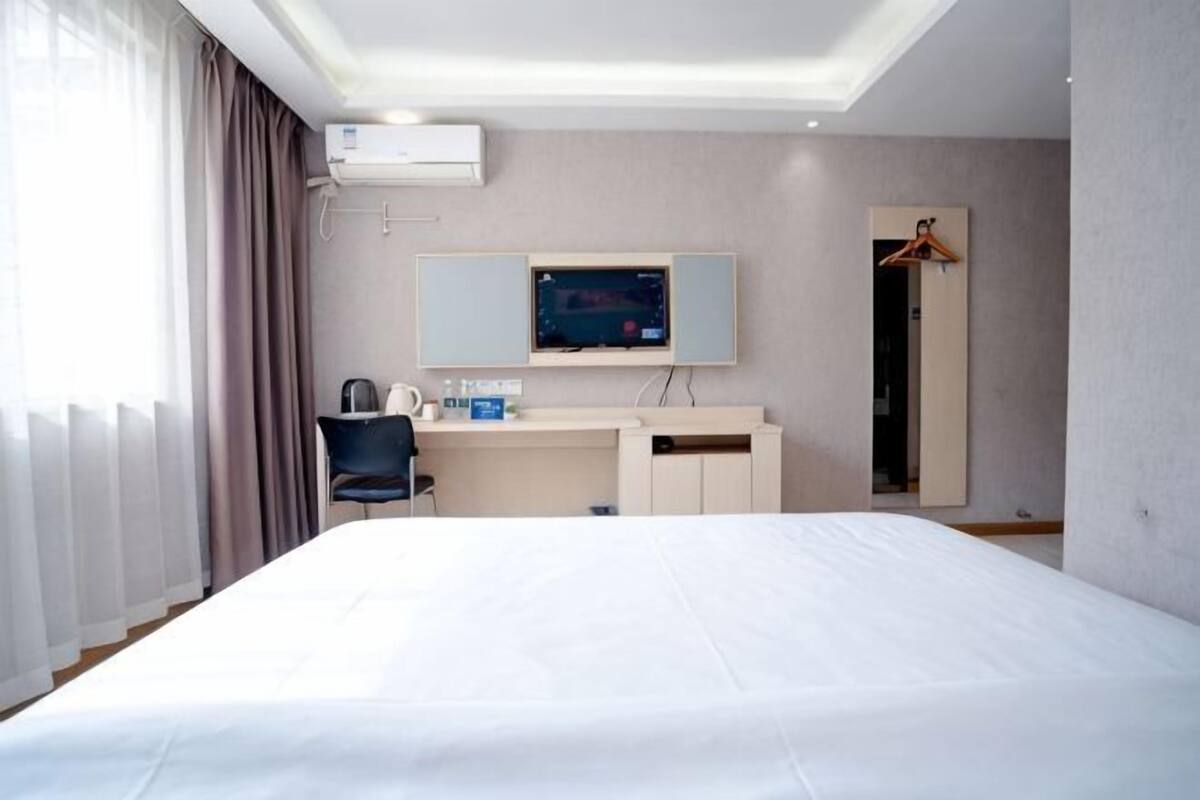 A hotel room with a bed, a desk, a chair, a television, and a mirror.