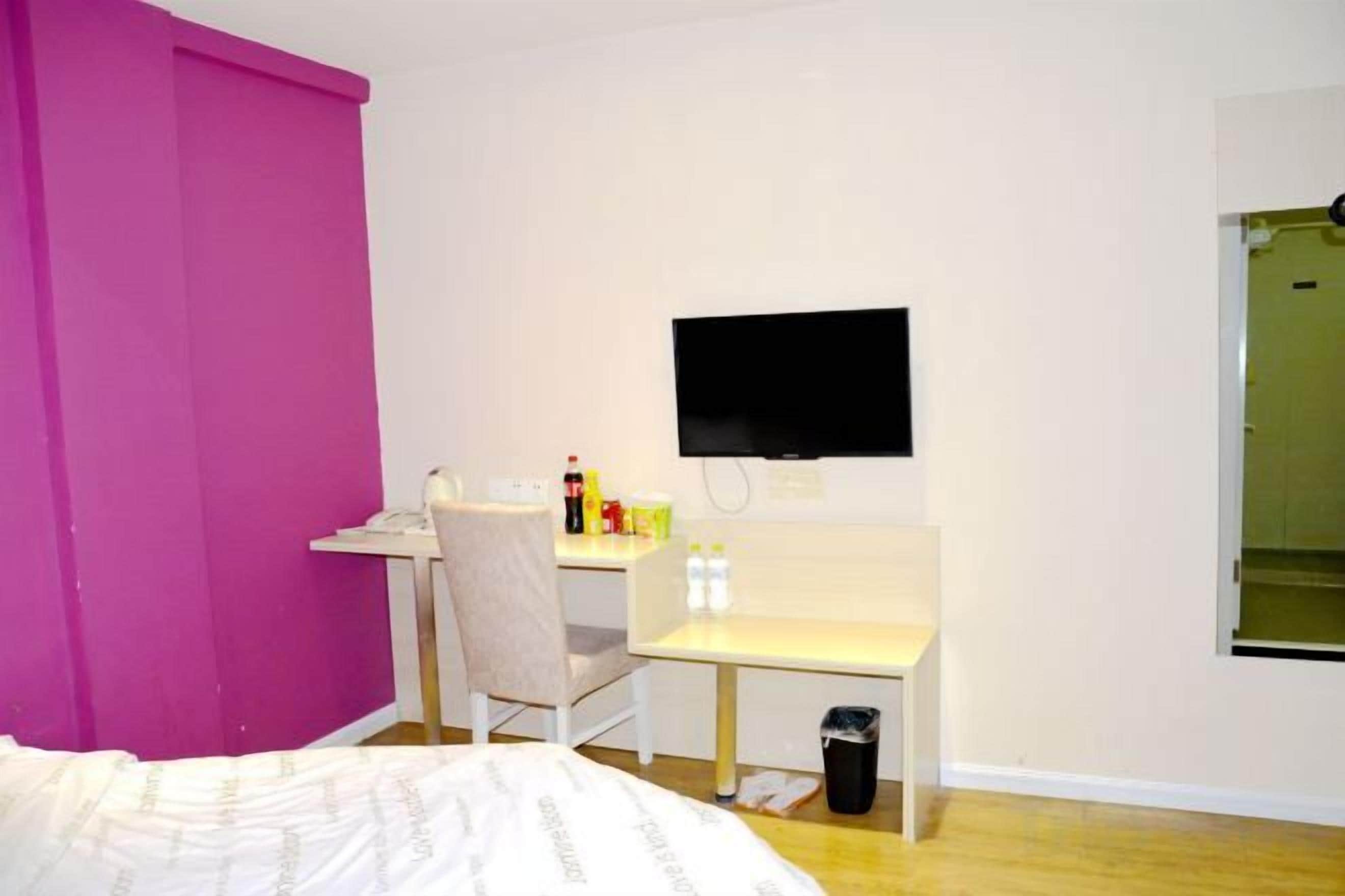 A bedroom with a bed, a desk, a chair, a TV, and a trash bin.