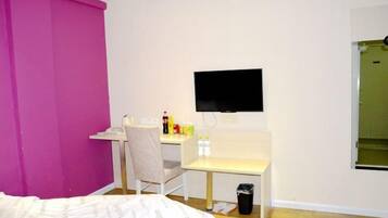 A bedroom with a bed, a desk, a chair, a TV, and a trash bin.