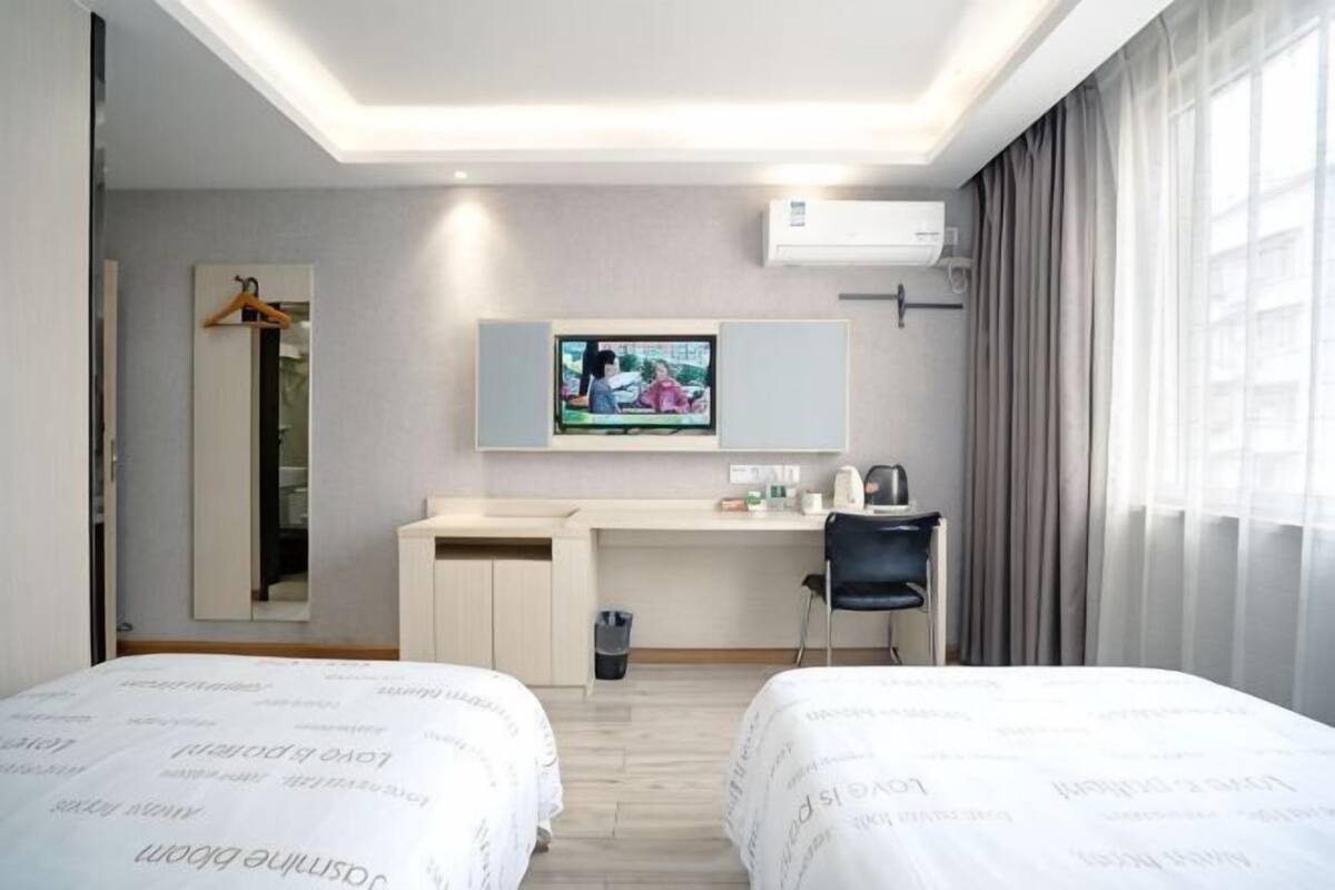 A hotel room with two beds, a desk, a chair, a TV, and a mirror.