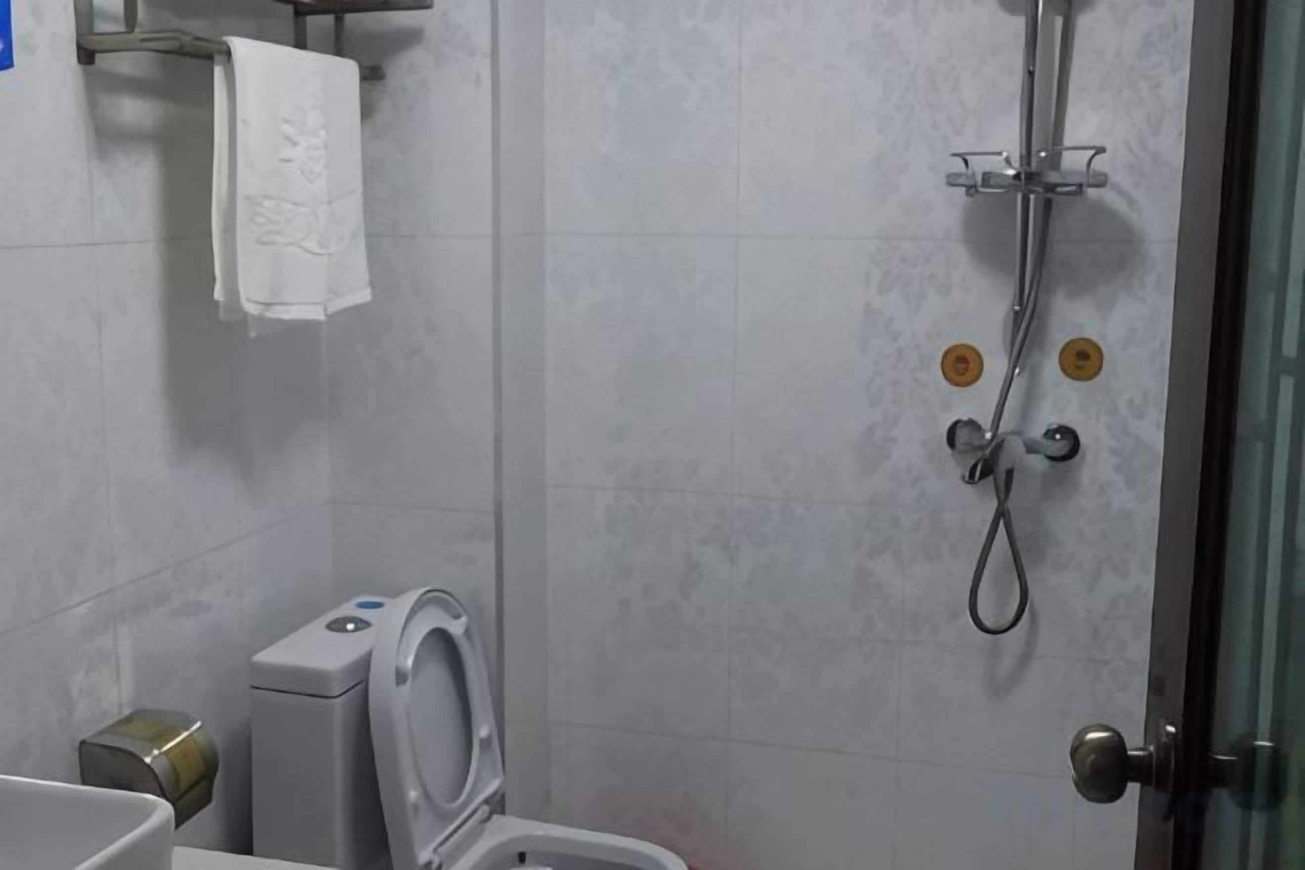 A bathroom with a toilet, a shower, and a towel hanging on the wall.