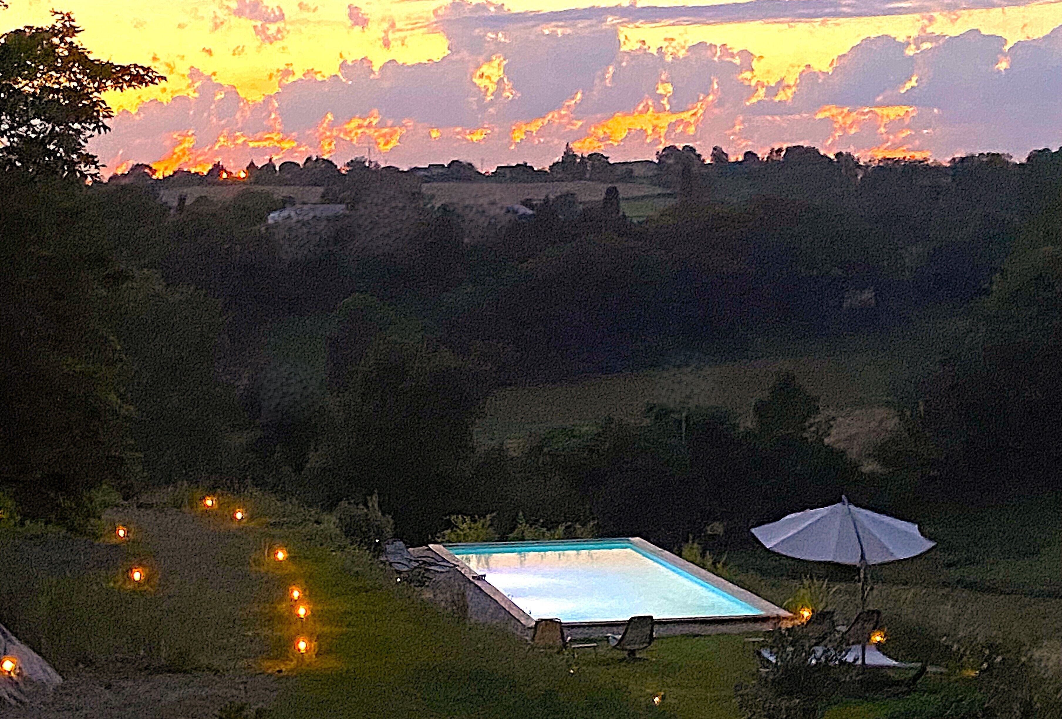 A rectangular pool with a clear blue water surface, surrounded by a grassy area with a few chairs and an umbrella.