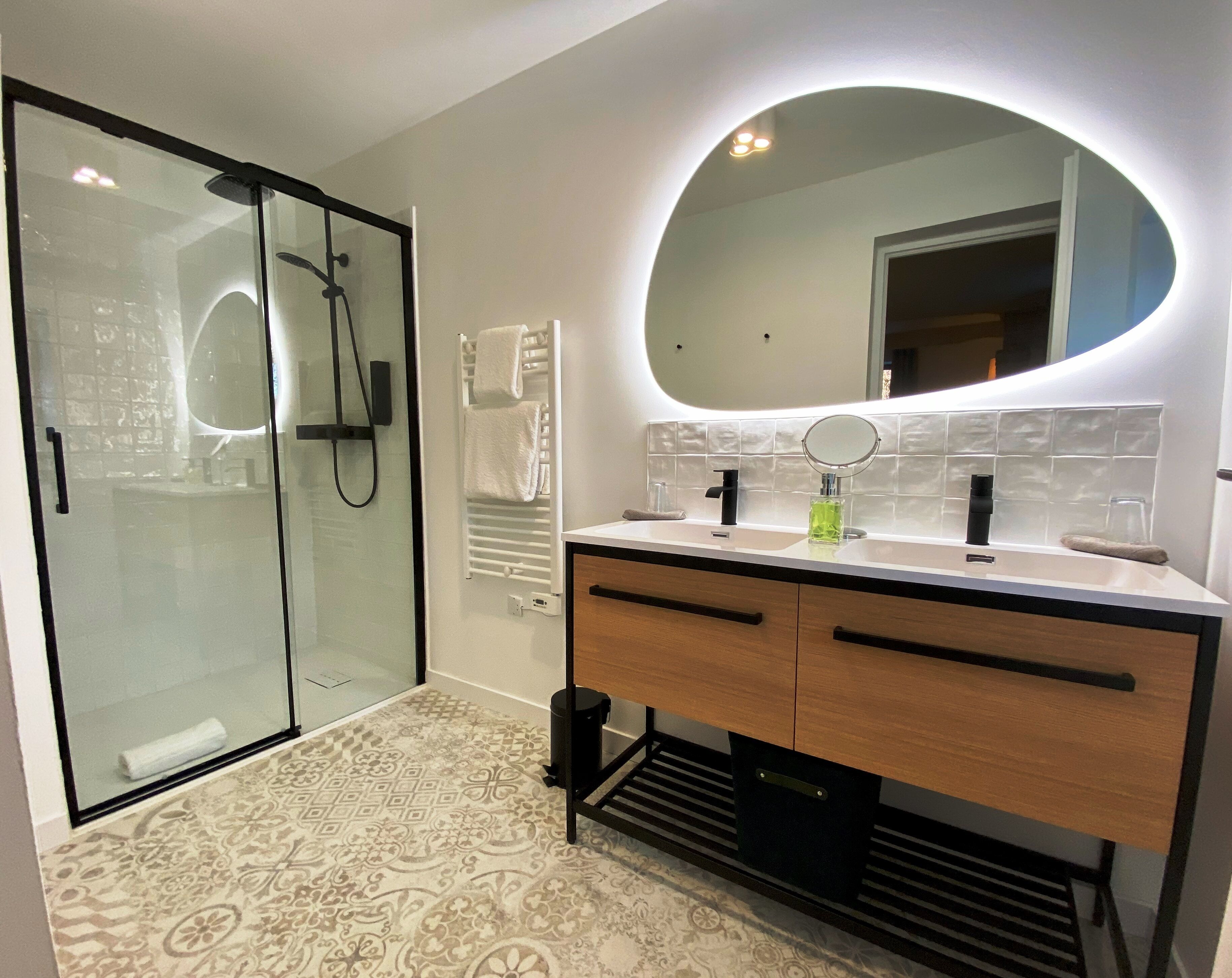 Un bagno moderno con cabina doccia in vetro, un mobile lavabo con specchio e un pavimento decorato.
