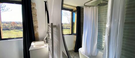 Een badkamer met een bad, een wastafel en een raam met uitzicht op een groen landschap.