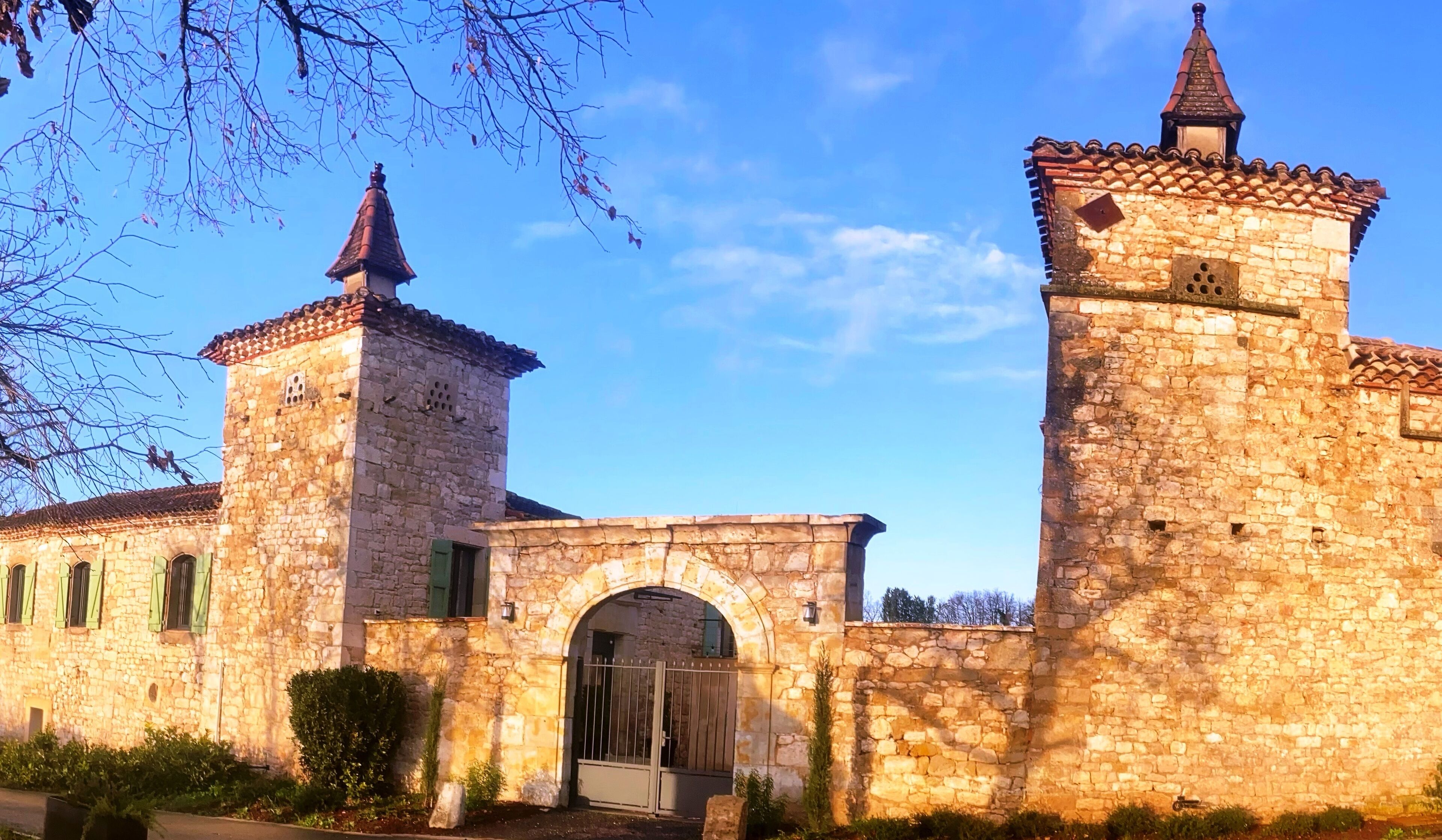 A historic stone building with a central archway and two towers, one with a pointed roof and the other with a conical roof.