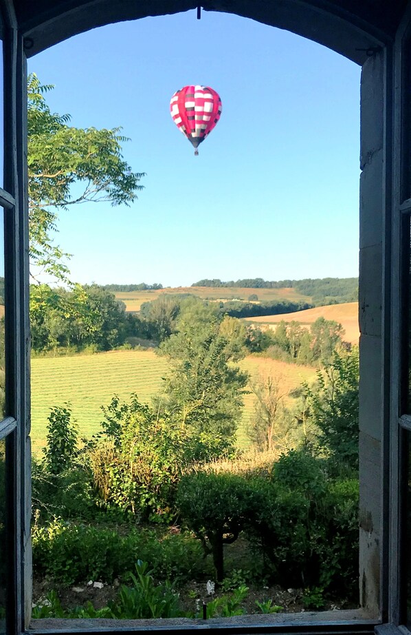 A view through an arched window of a countryside landscape with a hot air balloon in the sky. - DOMAINE DE LEJOS - Portes d'Albi (Lamillarie)