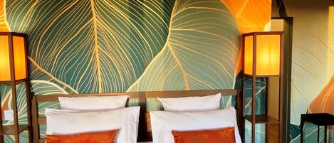 Habitación de hotel con una cama grande, dos almohadas, un cabecero y una pared con diseño de hojas. Hay dos lámparas a cada lado de la cama.