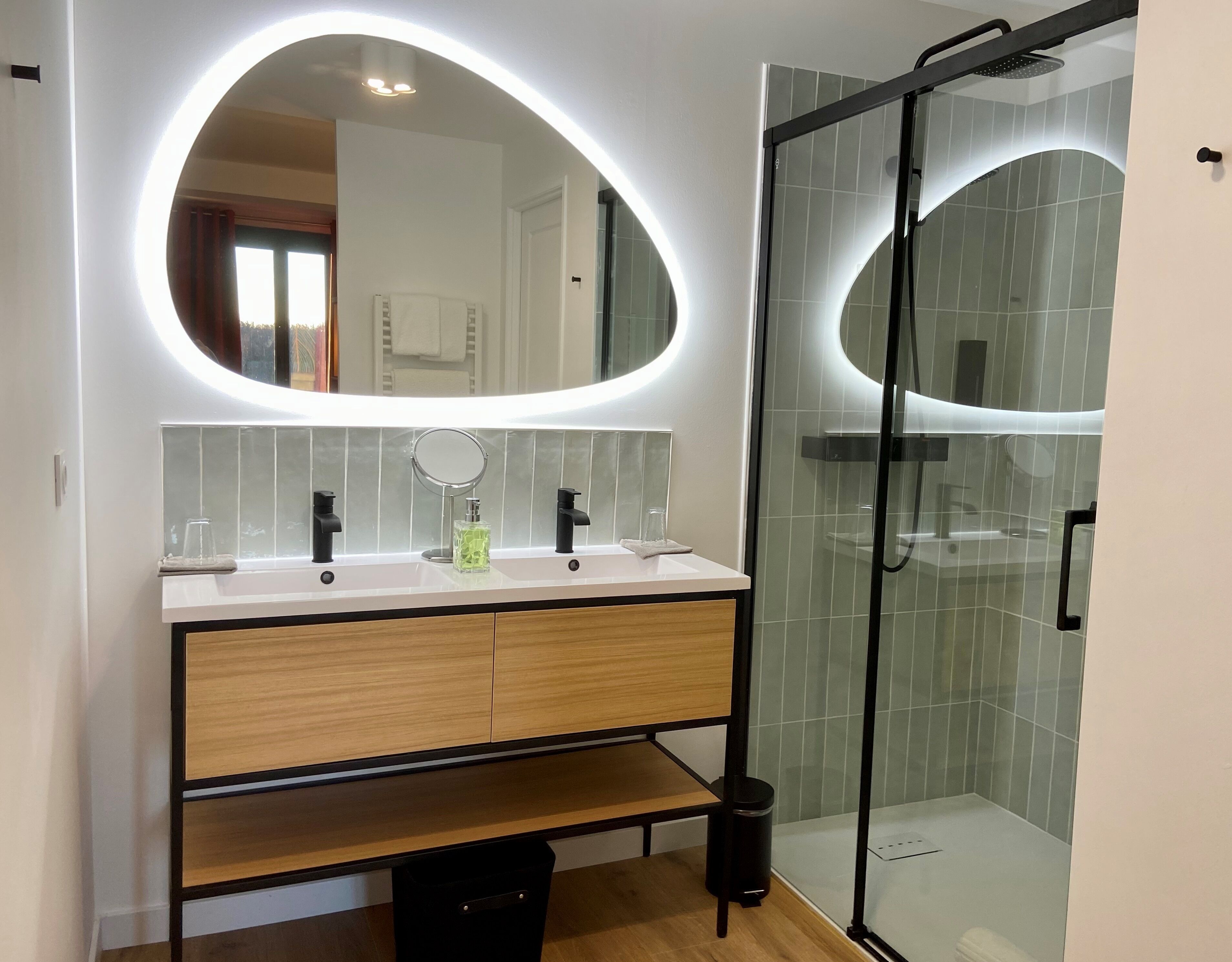 Un baño moderno con tocador, dos lavamanos, espejo y ducha con cerramiento de vidrio.
