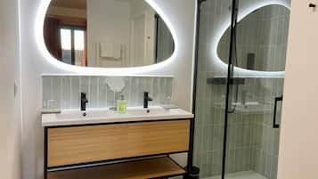 Un baño moderno con tocador, dos lavamanos, espejo y ducha con cerramiento de vidrio.